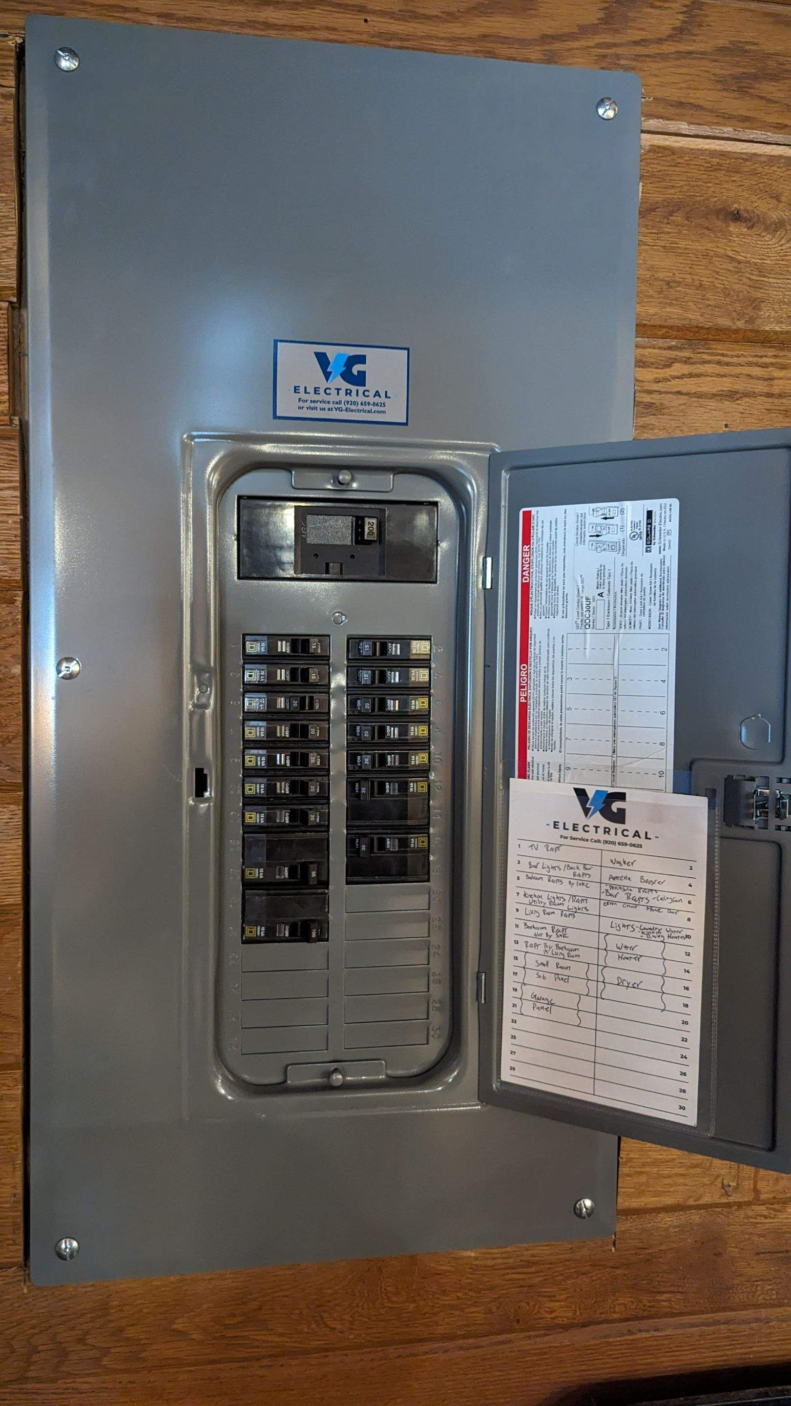 A electrical panel is sitting on a wooden floor with the door open.