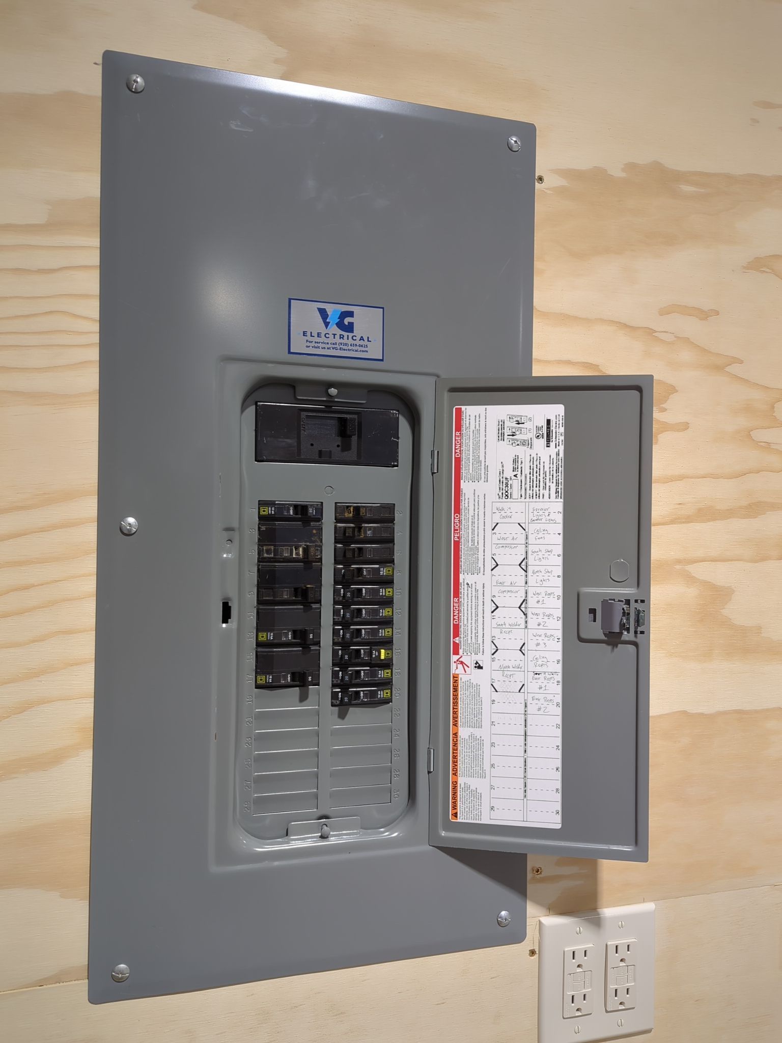 A gray electrical box with the lid open on a wooden wall