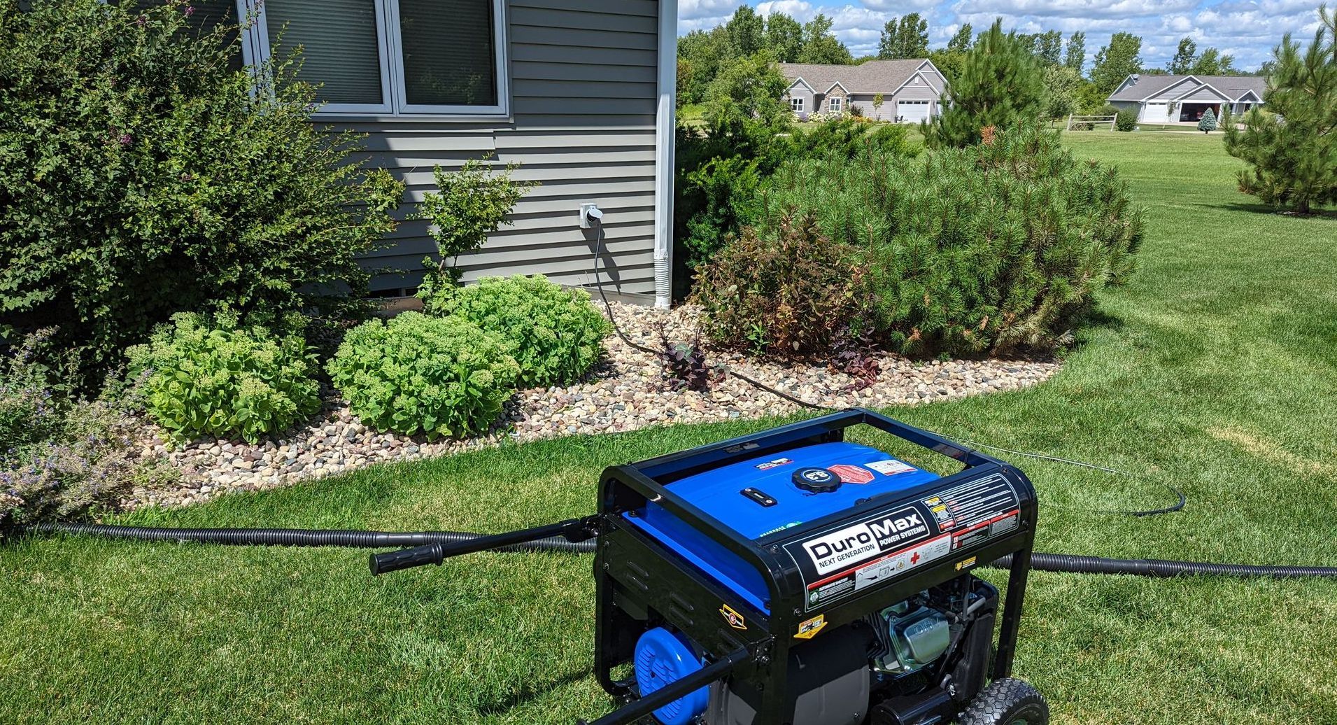 A generator is sitting in the grass in front of a house.