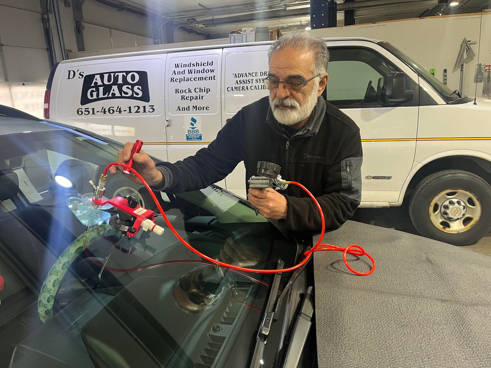 A man is fixing a windshield on a car in front of a van.