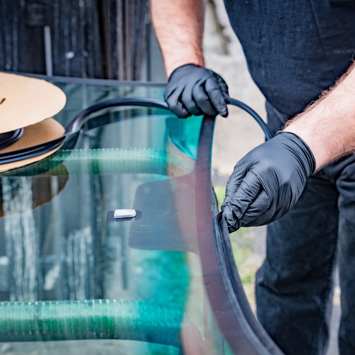 A man wearing black gloves is working on a windshield.