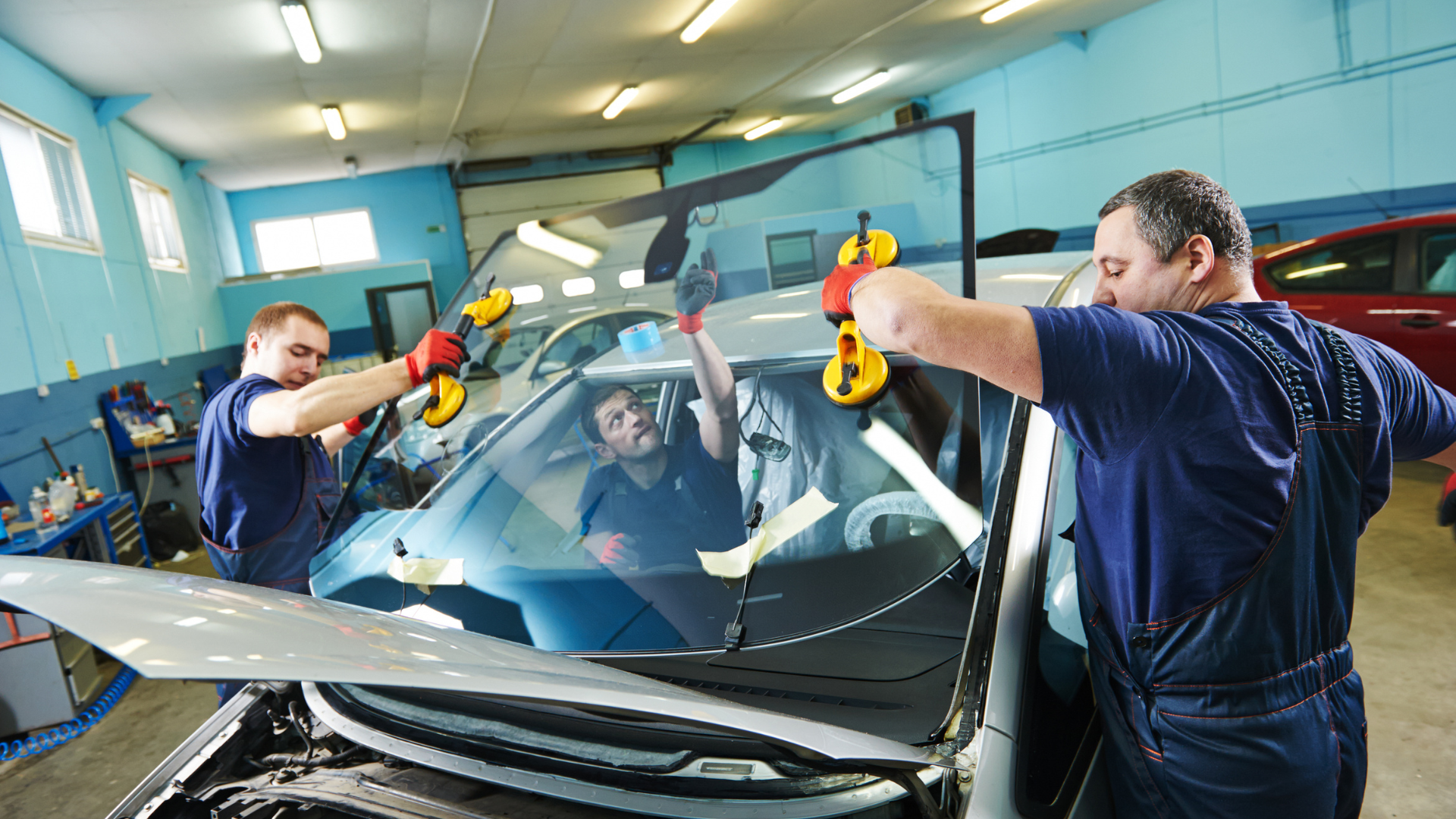 Three men are installing a windshield on a car in a garage.