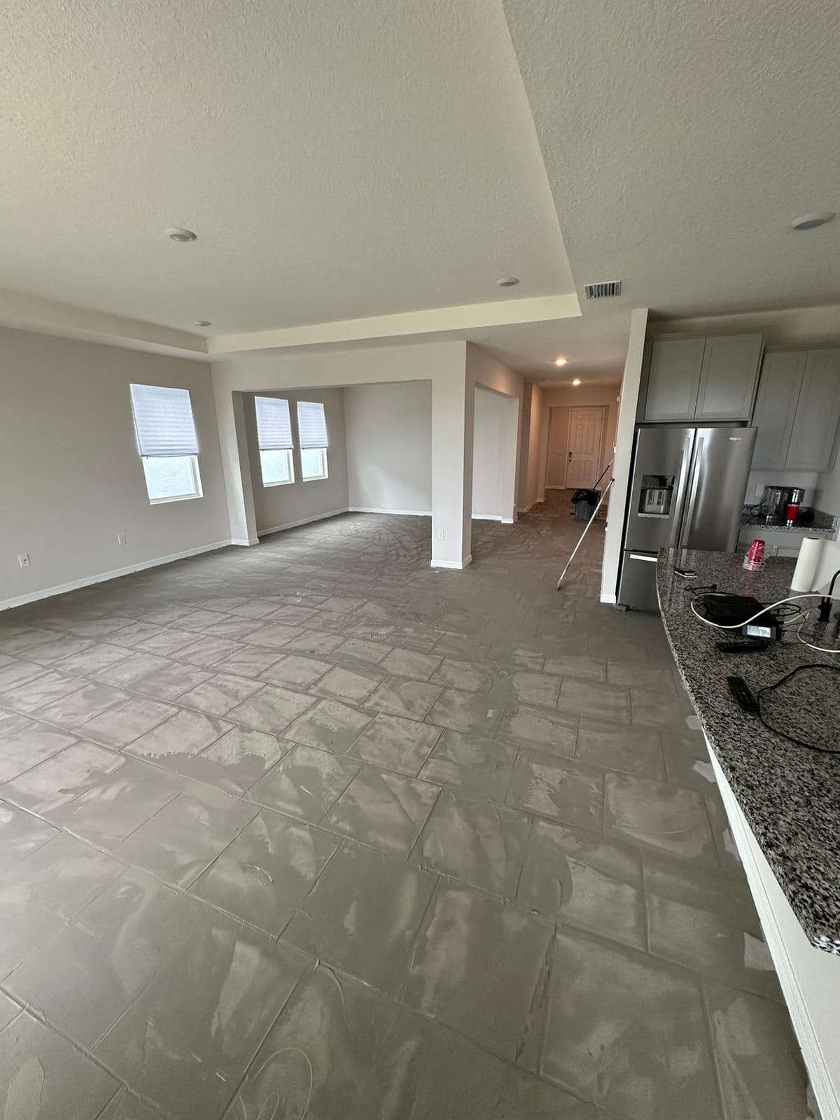 A large empty room with a tiled floor and a kitchen in the background.