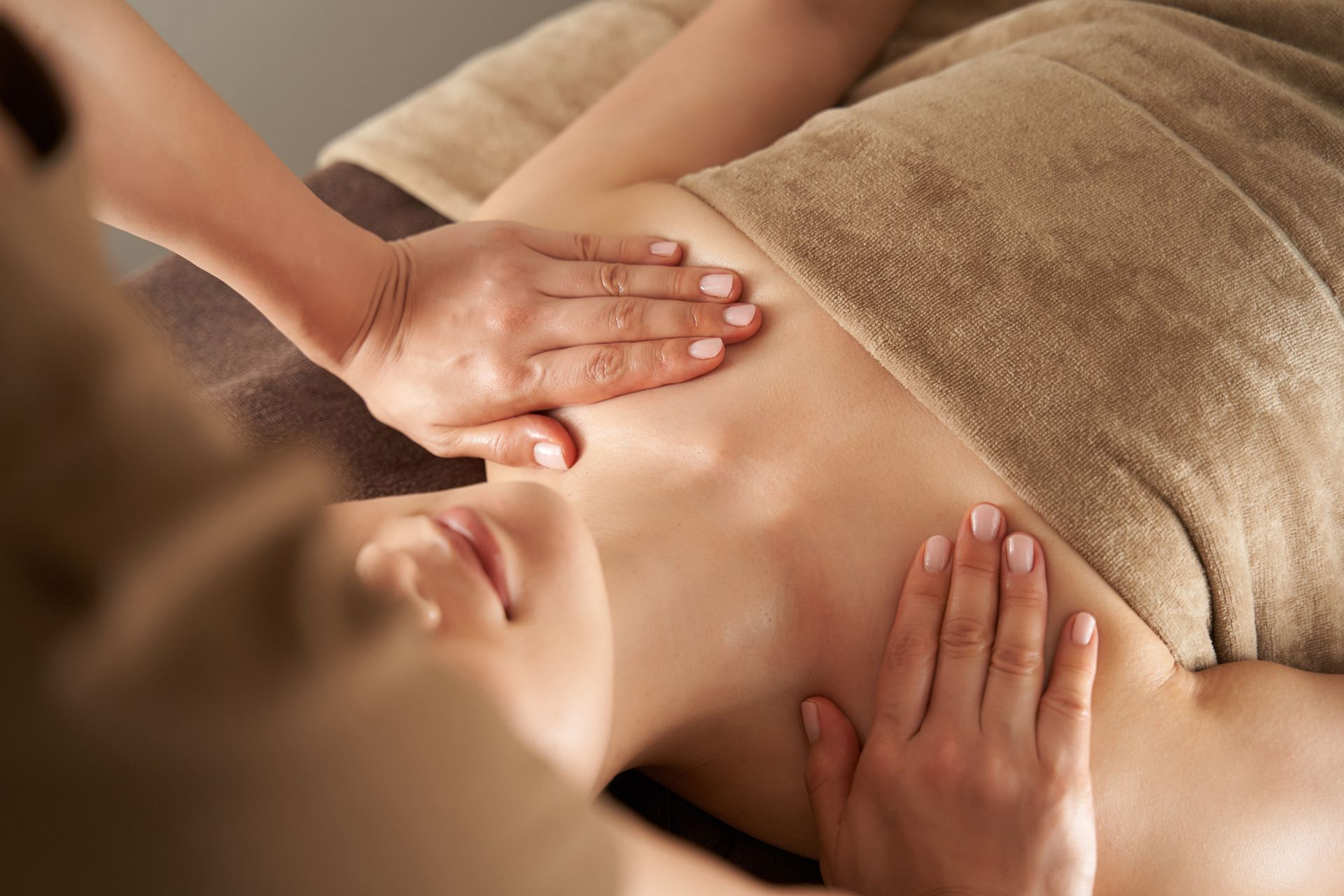 Woman receiving a chest massage at a spa; hands on chest, tan towel.
