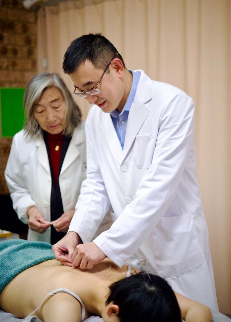 Two doctors are giving acupuncture to a patient