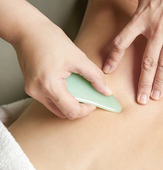 a woman is getting a massage with a green gua sha tool .
