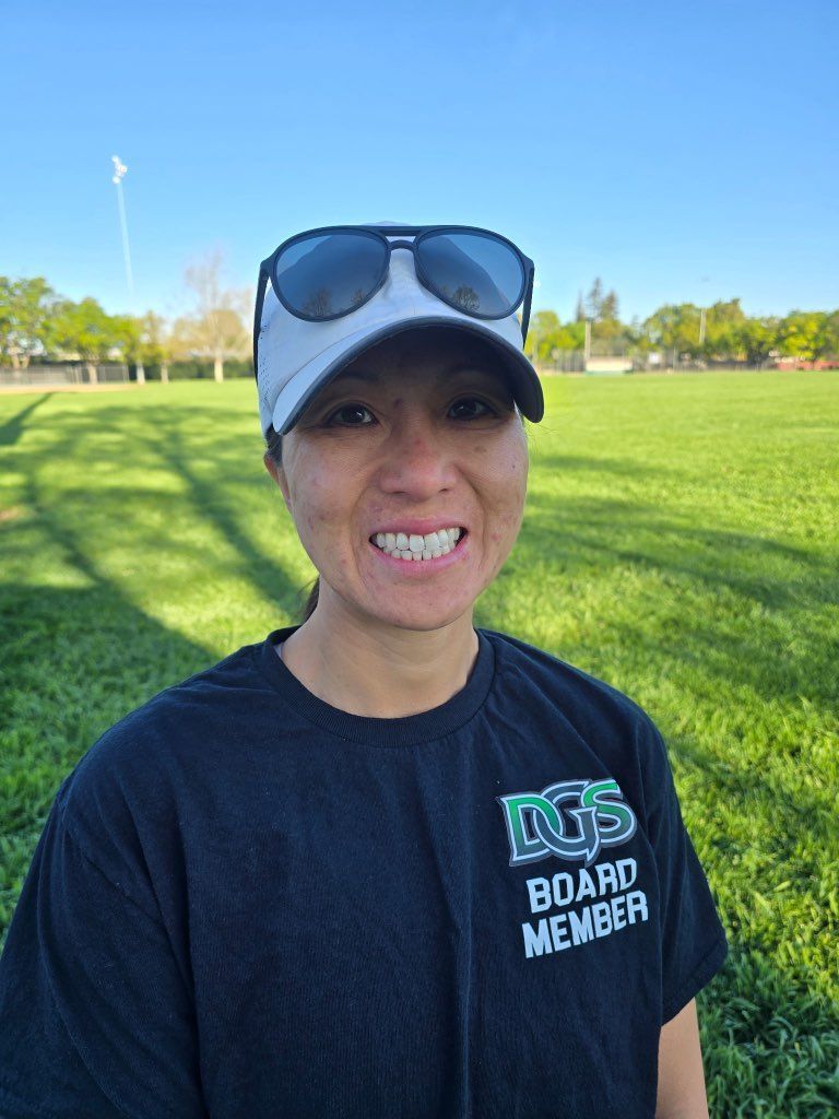Man in green polo stands on a football field, arms crossed, stadium in background.