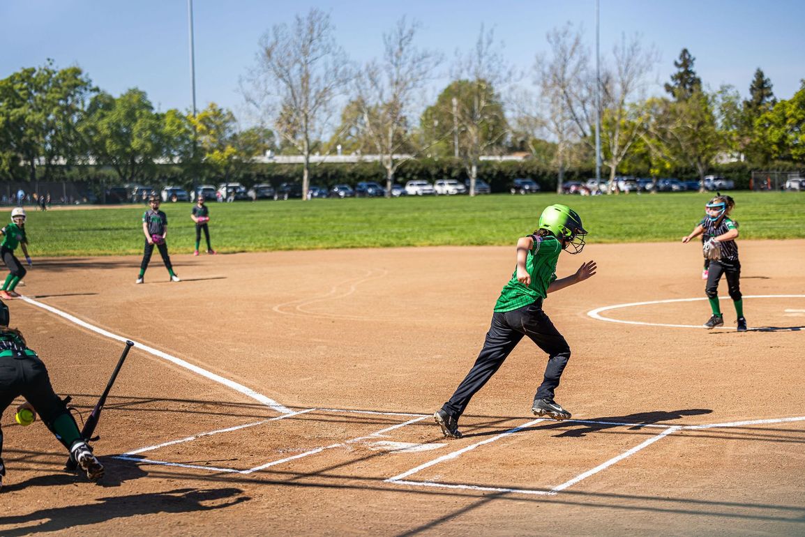 A person wearing a hat and orange shirt, holding a baseball bat on their shoulder on a baseball field.
