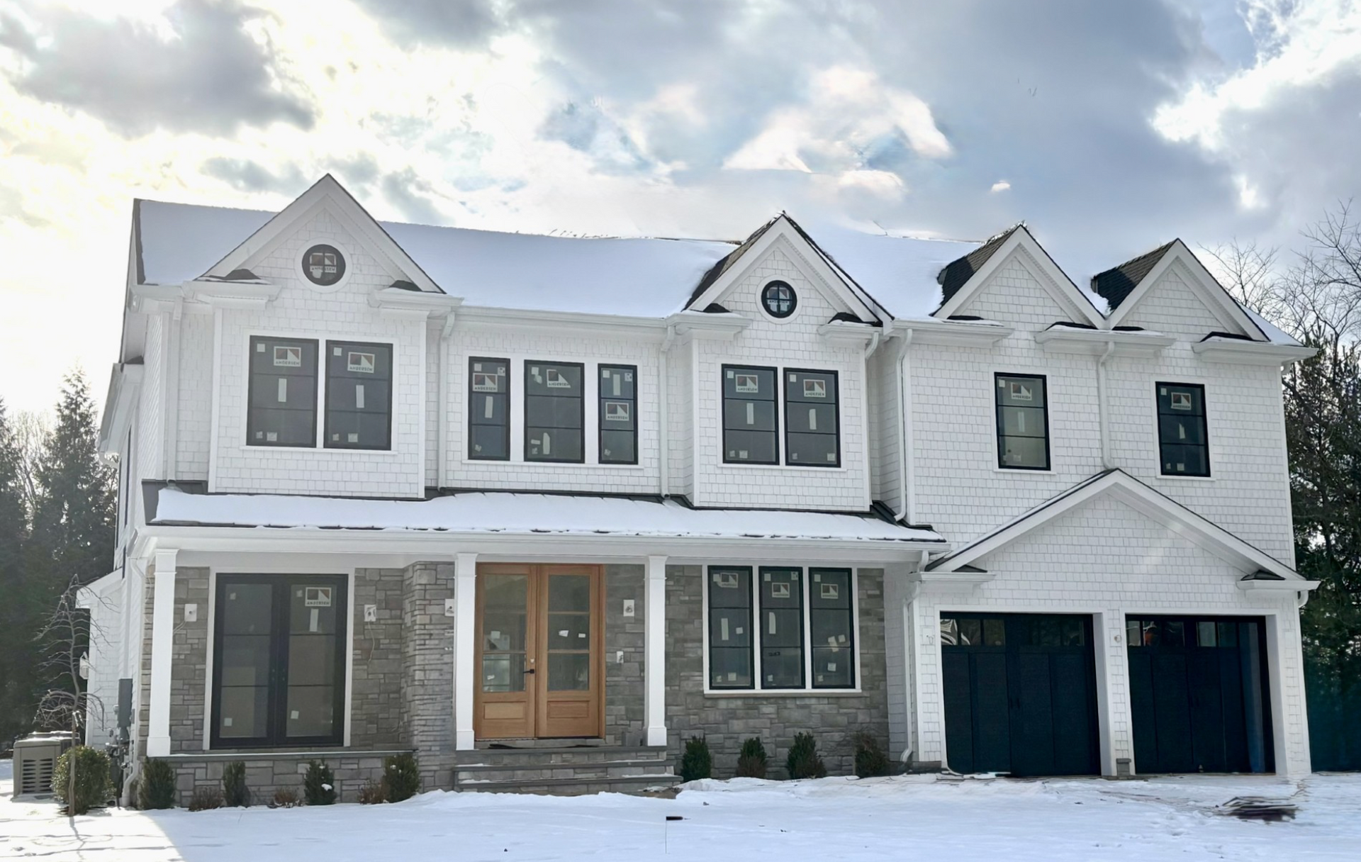 A large white house with black garage doors is covered in snow.
