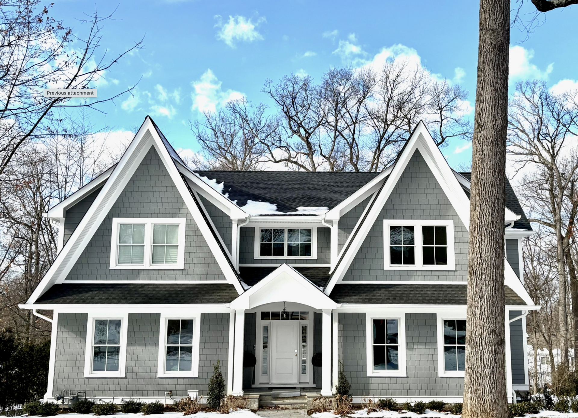 A large gray and white house is surrounded by snow and trees.