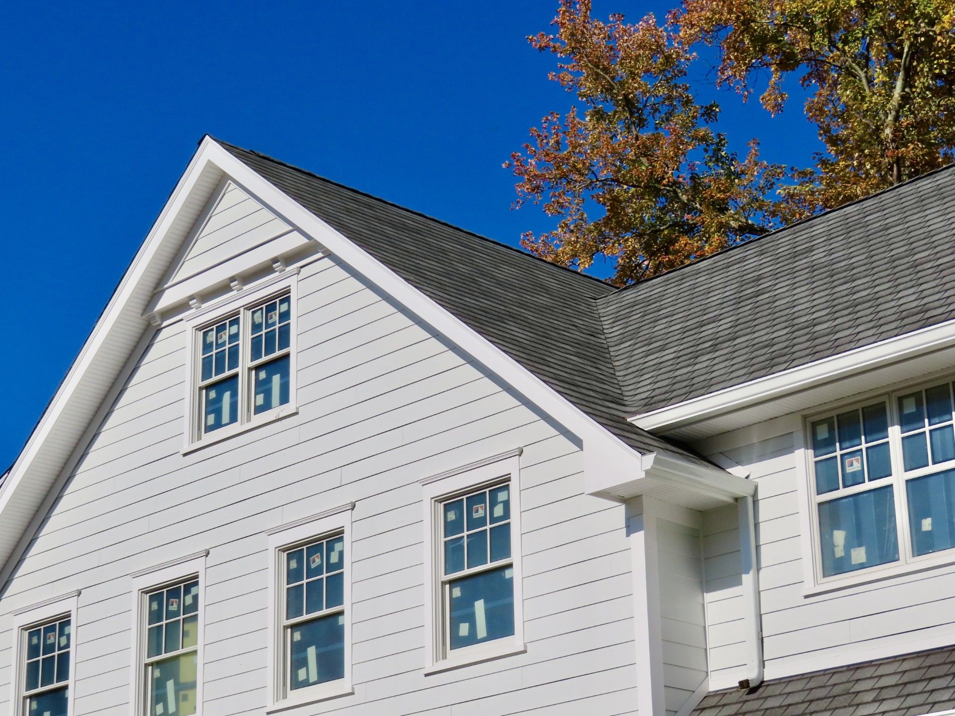 A white house with a gray roof and a tree in the background