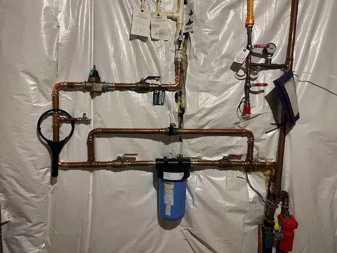 Copper pipes and water filter system against white wall.