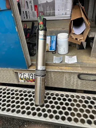 A long, silver, cylindrical water sensor with wires, sitting on a metal surface next to tools and documents.