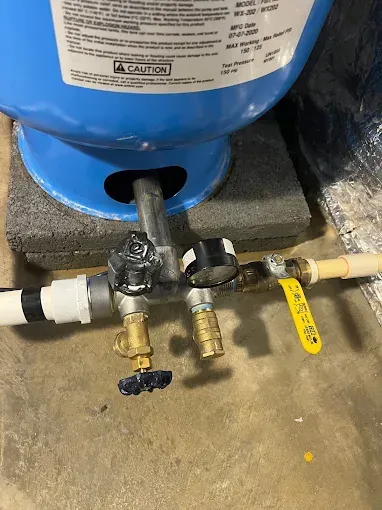 Blue water tank with plumbing, valves, and pipes on a concrete floor.