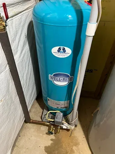 A tall, blue Well-Rite water pressure tank in a utility room, with copper pipes and a control box.