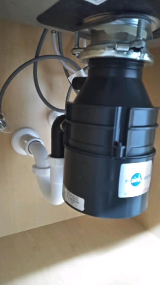 Garbage disposal unit under a sink with white pipes and gray tubing.