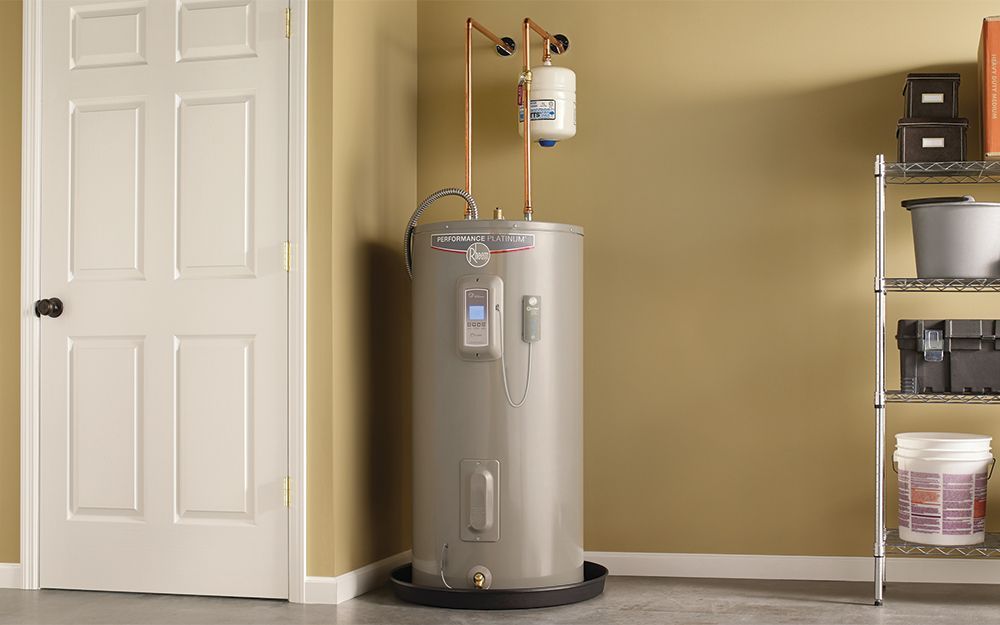 Water heater in a garage, next to a door and shelving unit.