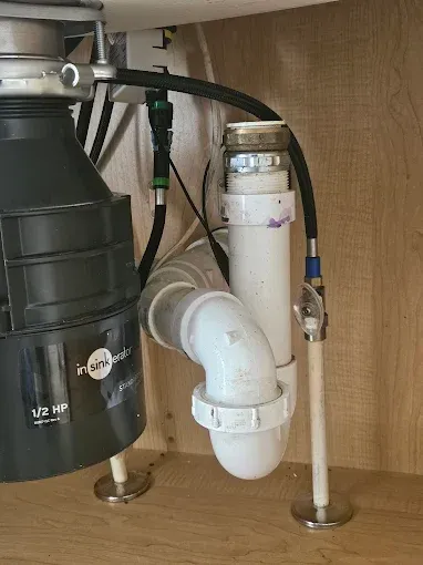 Under-sink plumbing with a garbage disposal, drain pipes, and water lines inside a cabinet.