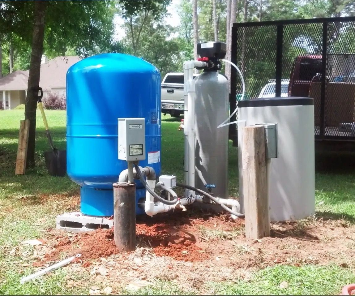 Blue water tank, water softener, and well components installed outdoors in a grassy area.