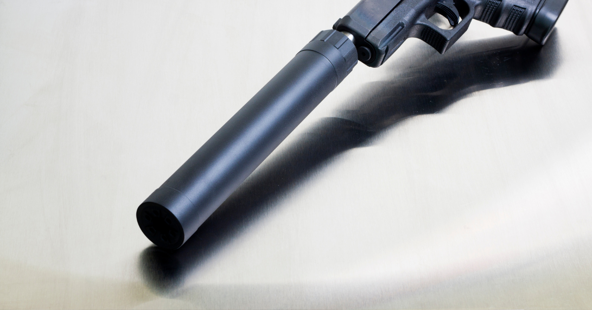 Black handgun with a silencer, resting on a reflective, metallic surface.