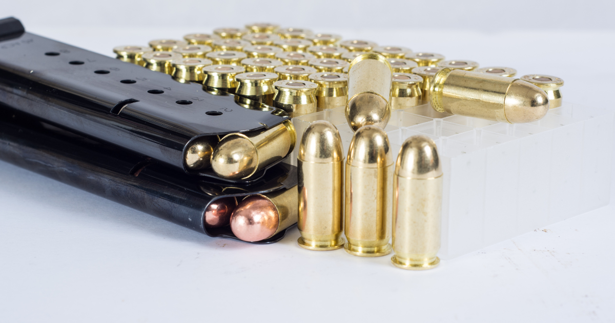A black handgun magazine next to brass-colored bullets, on a white surface.