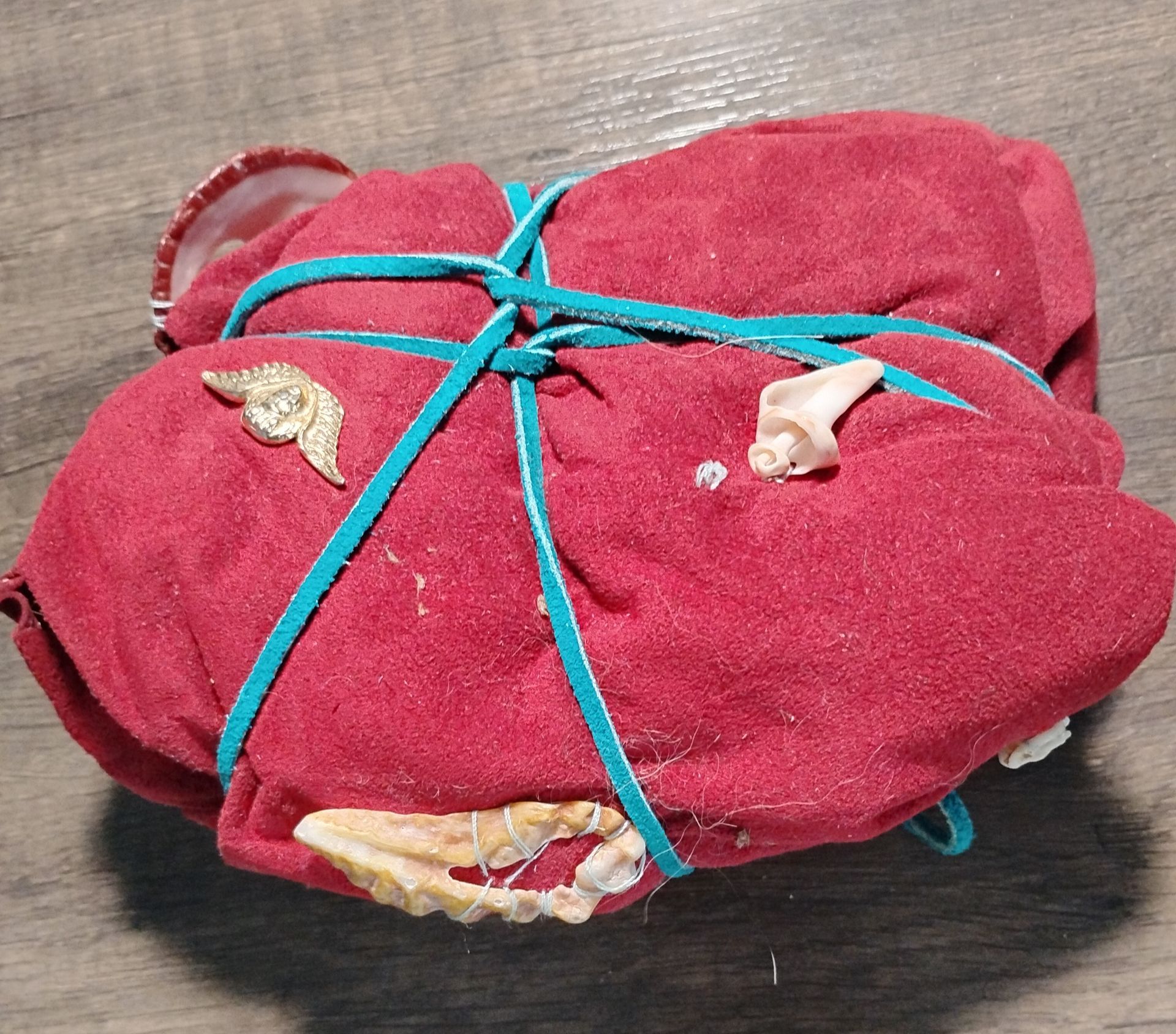 Red cloth bundle tied with teal rubber bands, containing bones and a gold-colored pin.