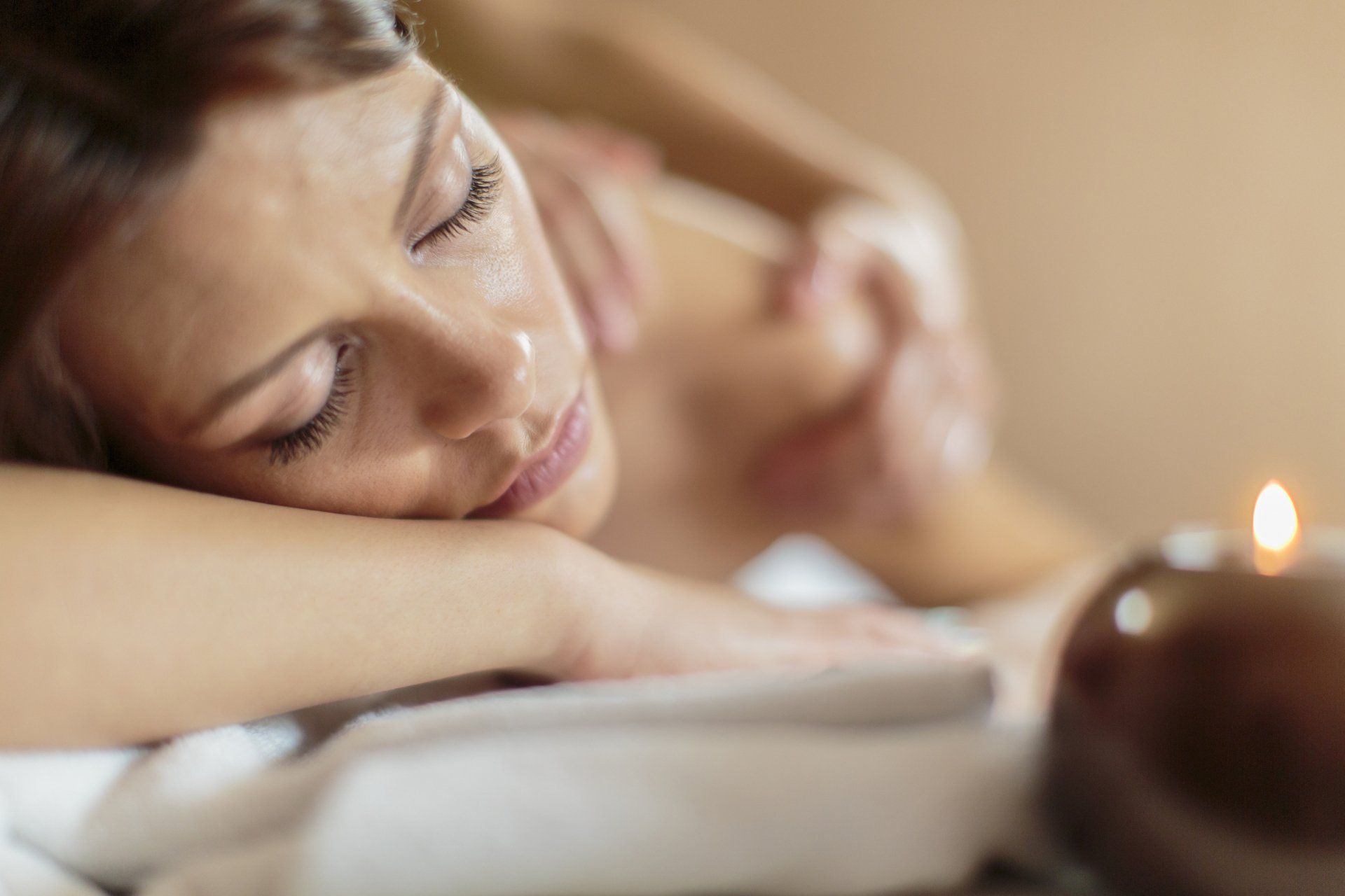 A woman is getting a massage in a spa with a candle in the background.