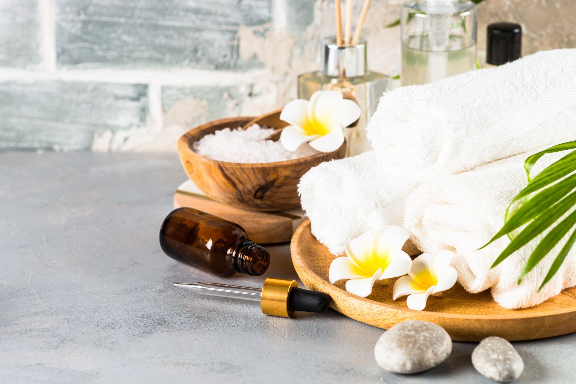 A wooden tray with towels , flowers , essential oils and rocks on a table.