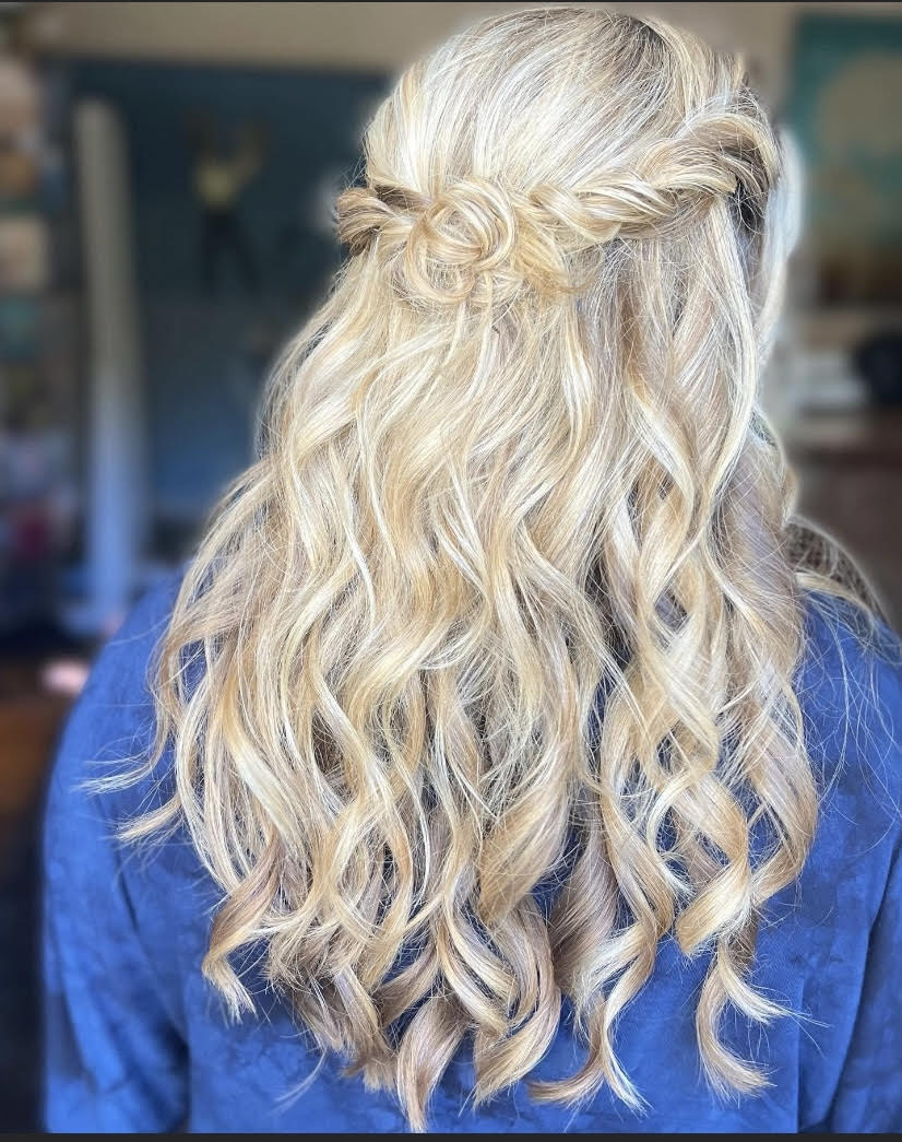 A woman with blonde hair is wearing a blue shirt and has her hair in a half up half down hairstyle.