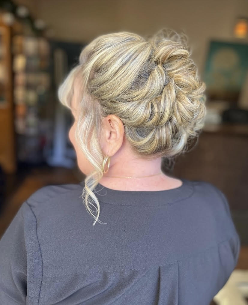 A woman with blonde hair in a messy bun is wearing a black shirt.