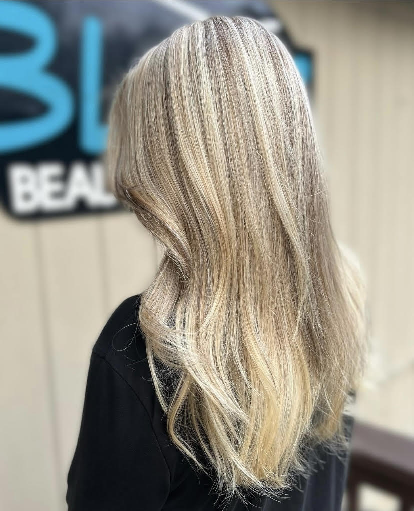 A woman with long blonde hair is standing in front of a building.