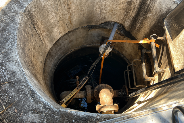 Workers descending into a dark manhole with ropes and tools inside a concrete shaft