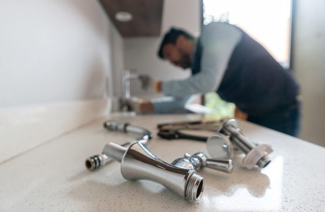 Shiny chrome faucet parts on a countertop with a blurred person working in the background