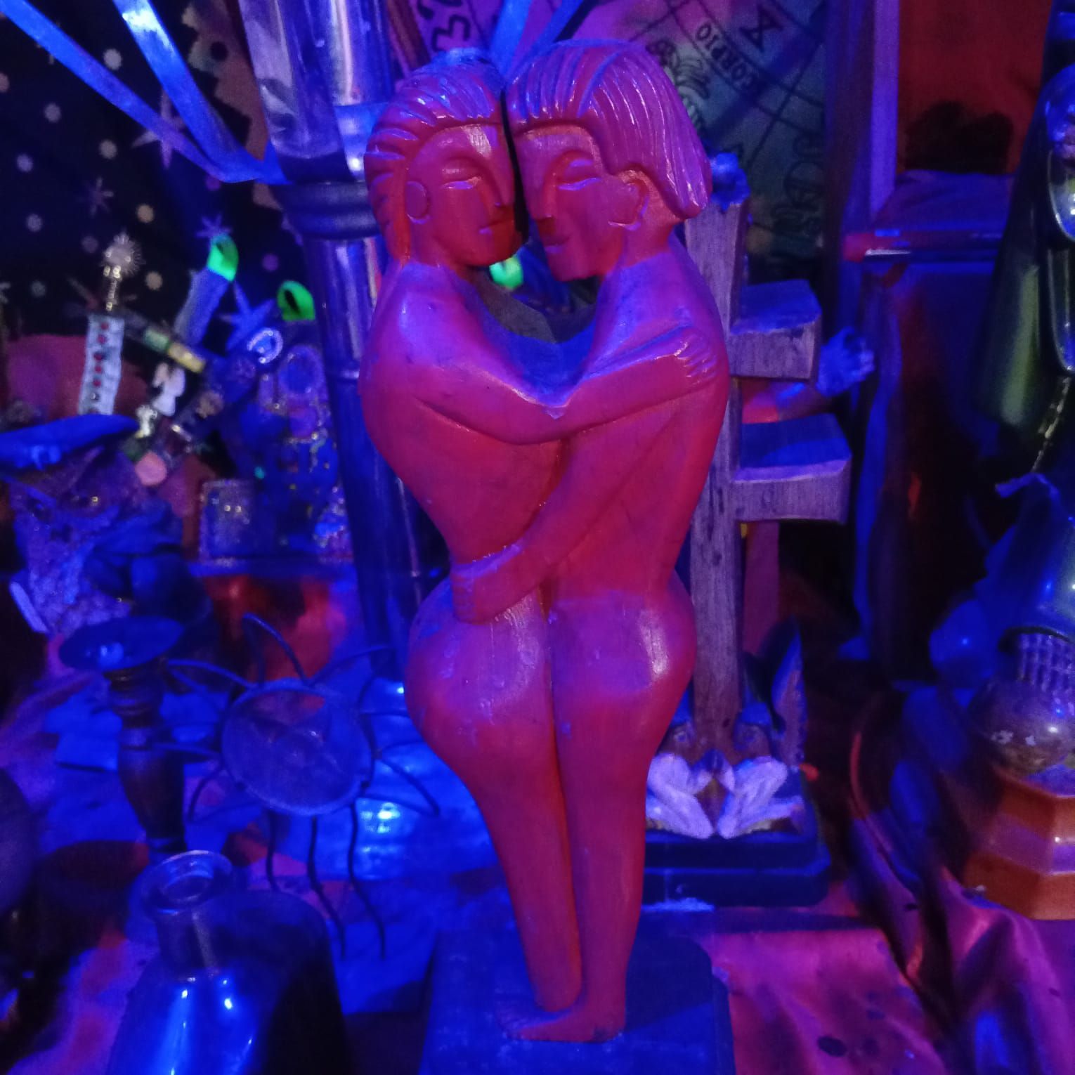 Talla de madera roja de dos figuras abrazándose en un entorno tenue y colorido.
