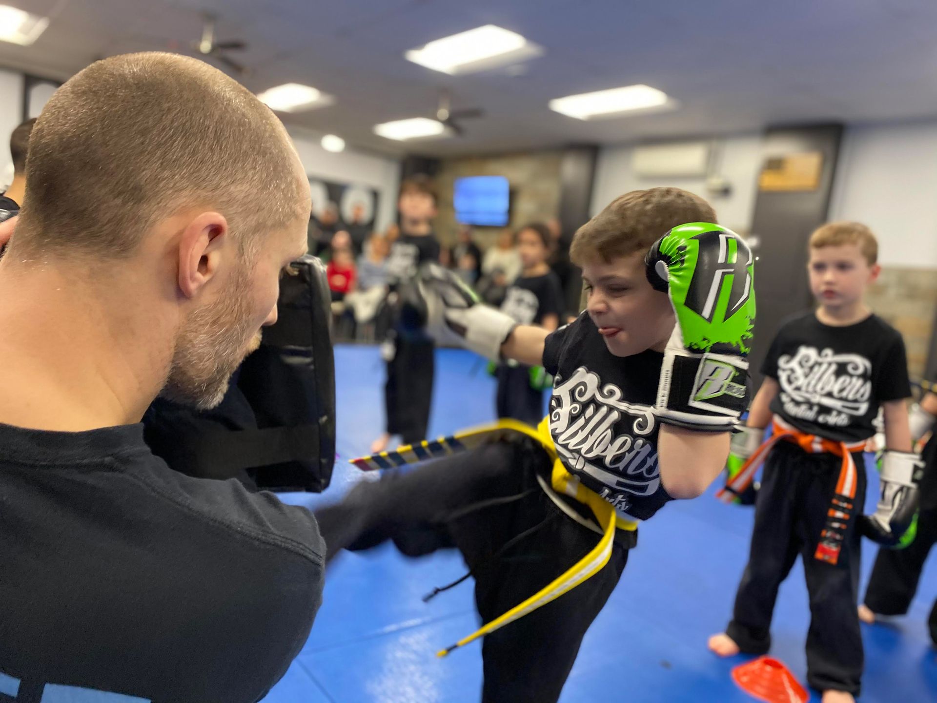 a man is teaching a young boy how to kick in a gym .