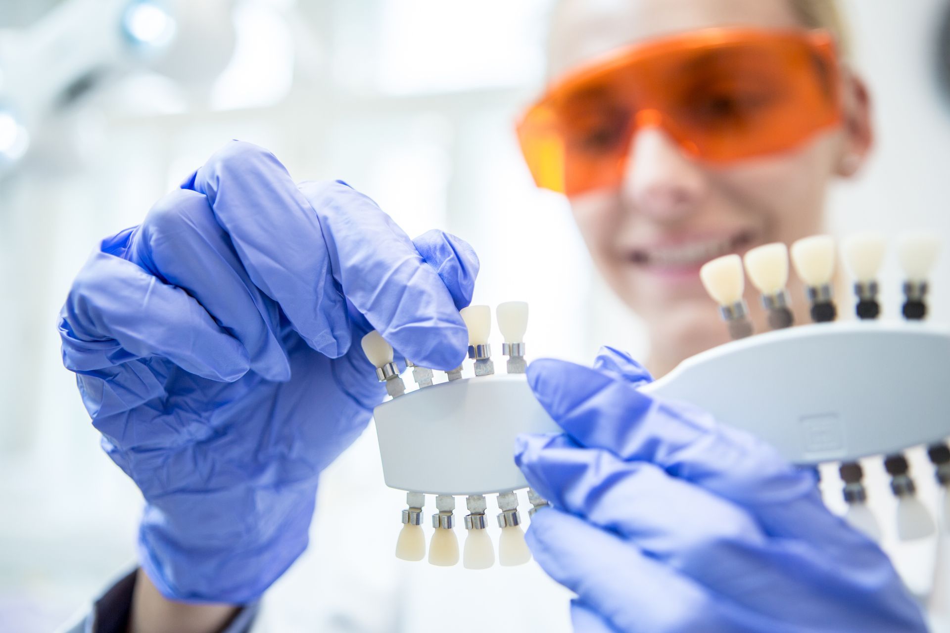 Dental implant shade matching by gloved dentist holding tooth color guide in bright clinic.