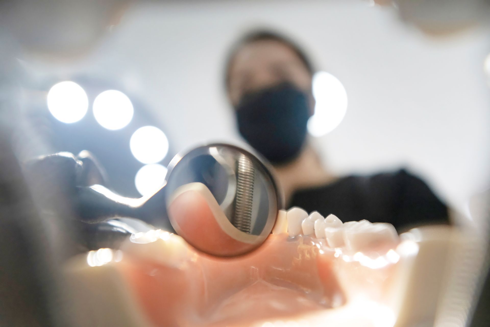 Inside a mouth: Dentist, wearing a mask, examines teeth with a mirror.