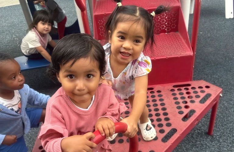 Happy Montessori toddlers playing on red playground equipment.