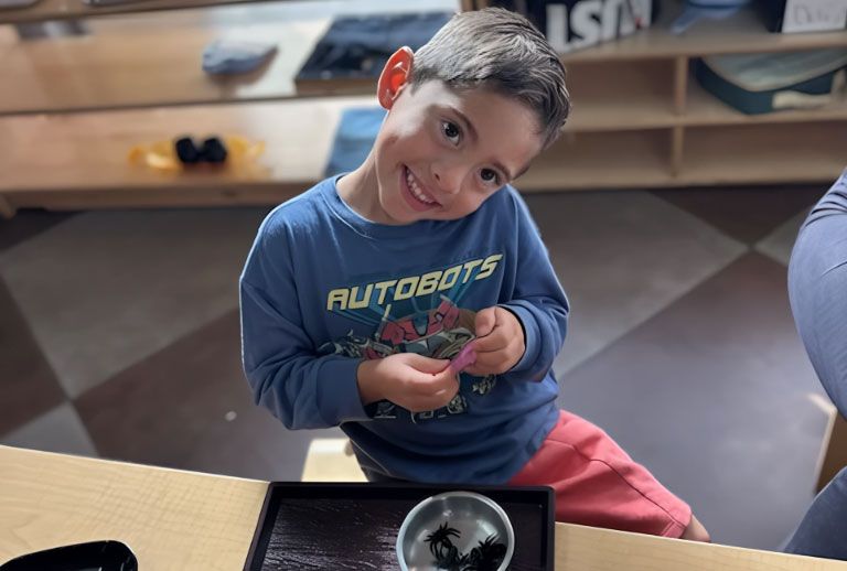 Smiling Montessori student working on a fine motor transfer activity.