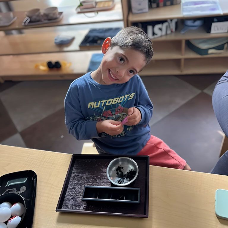 Smiling Montessori child working on fine motor cutting activity.
