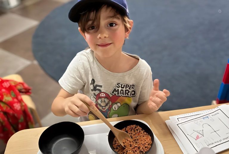 Smiling Montessori student doing a spooning transfer activity.