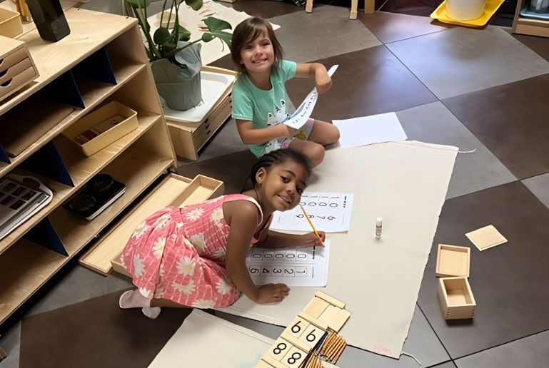 Two Montessori students working on numbers and counting with math materials on the floor.