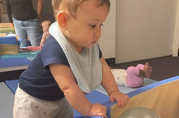 Montessori  infant pulling up on soft blocks in the Nido classroom.