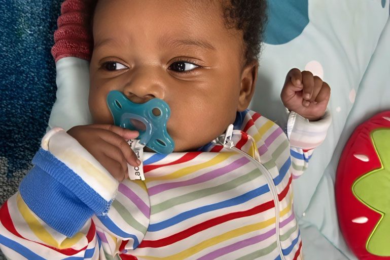 Montessori infant lying on a play mat with a pacifier in the classroom.