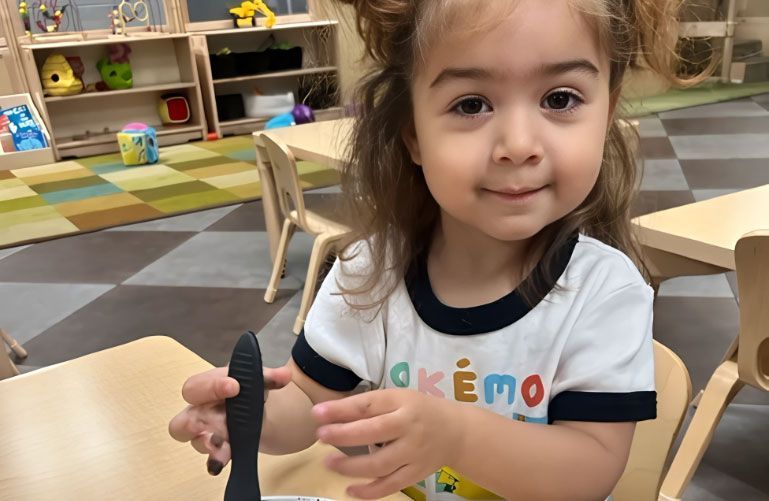 Montessori toddler smiling while painting with black paint and a tool.