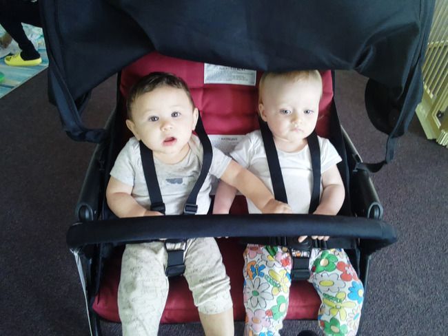 Two happy infants secured in a stroller in a Montessori toddler environmen