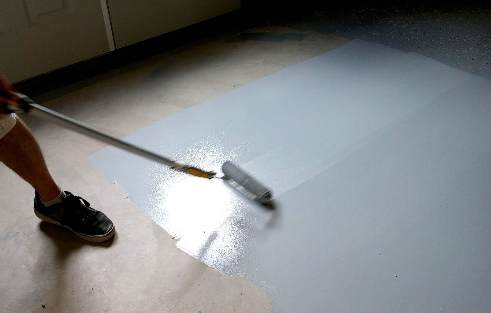 A person is painting a floor with a roller.