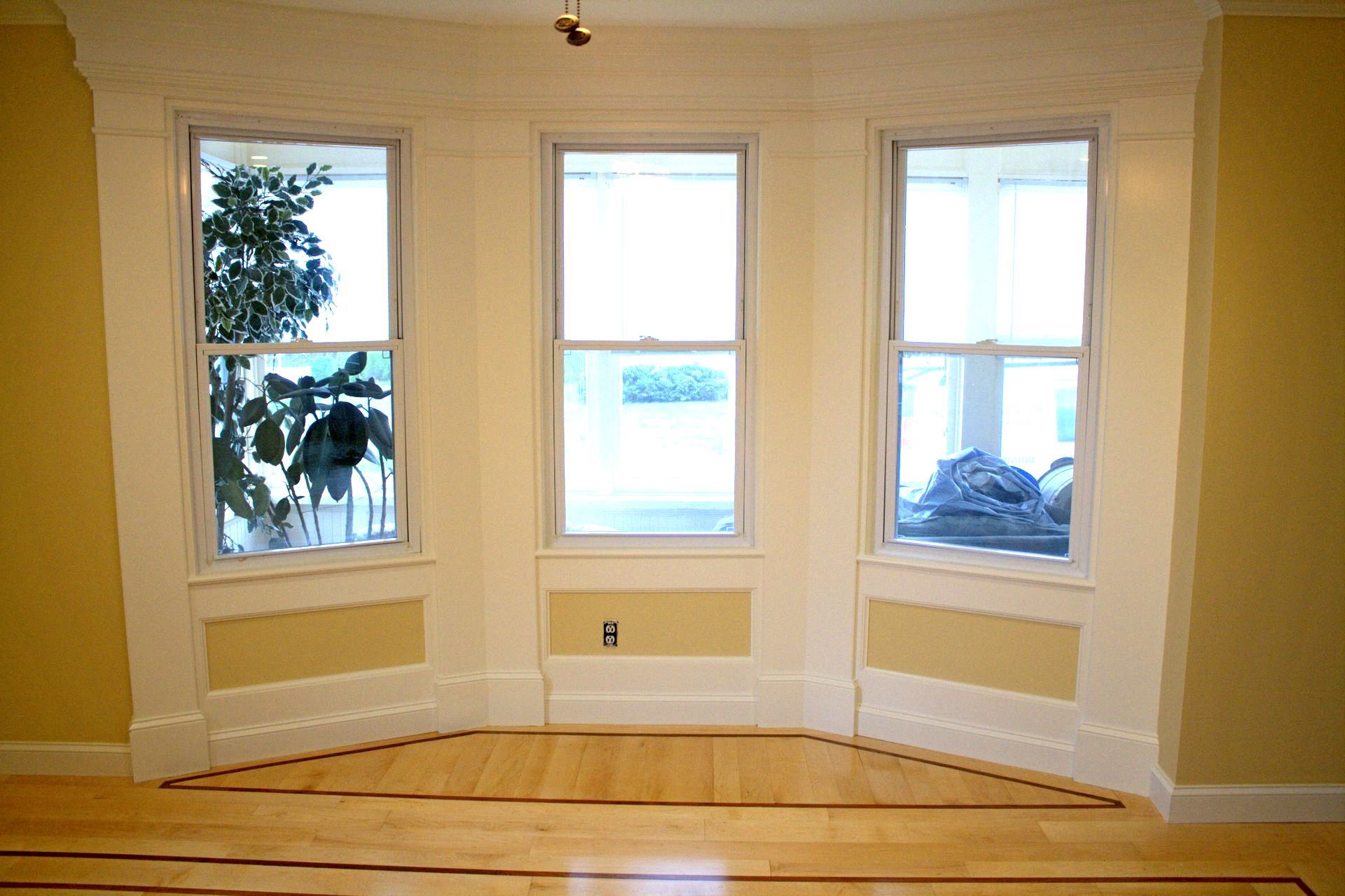 An empty room with three windows and a plant in the window