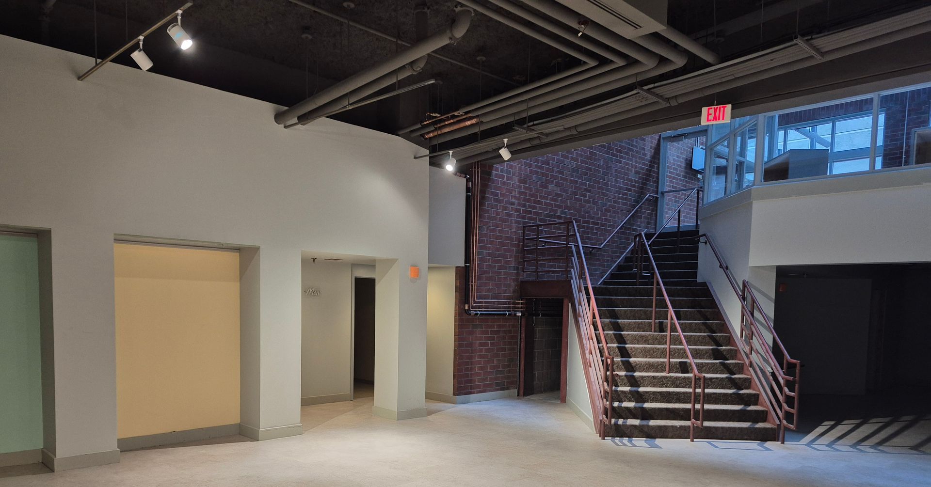 An empty room with stairs and a red exit sign