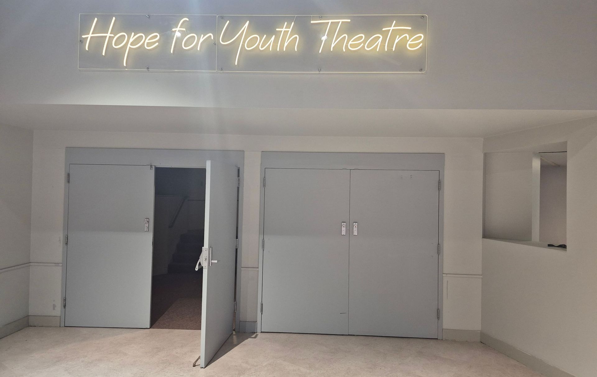 A room with a neon sign that says hope for youth theatre